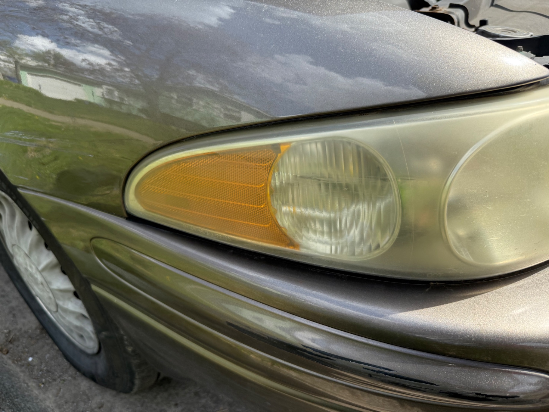 Angled view of a yellowed, hazy headlight and amber marker lens before service